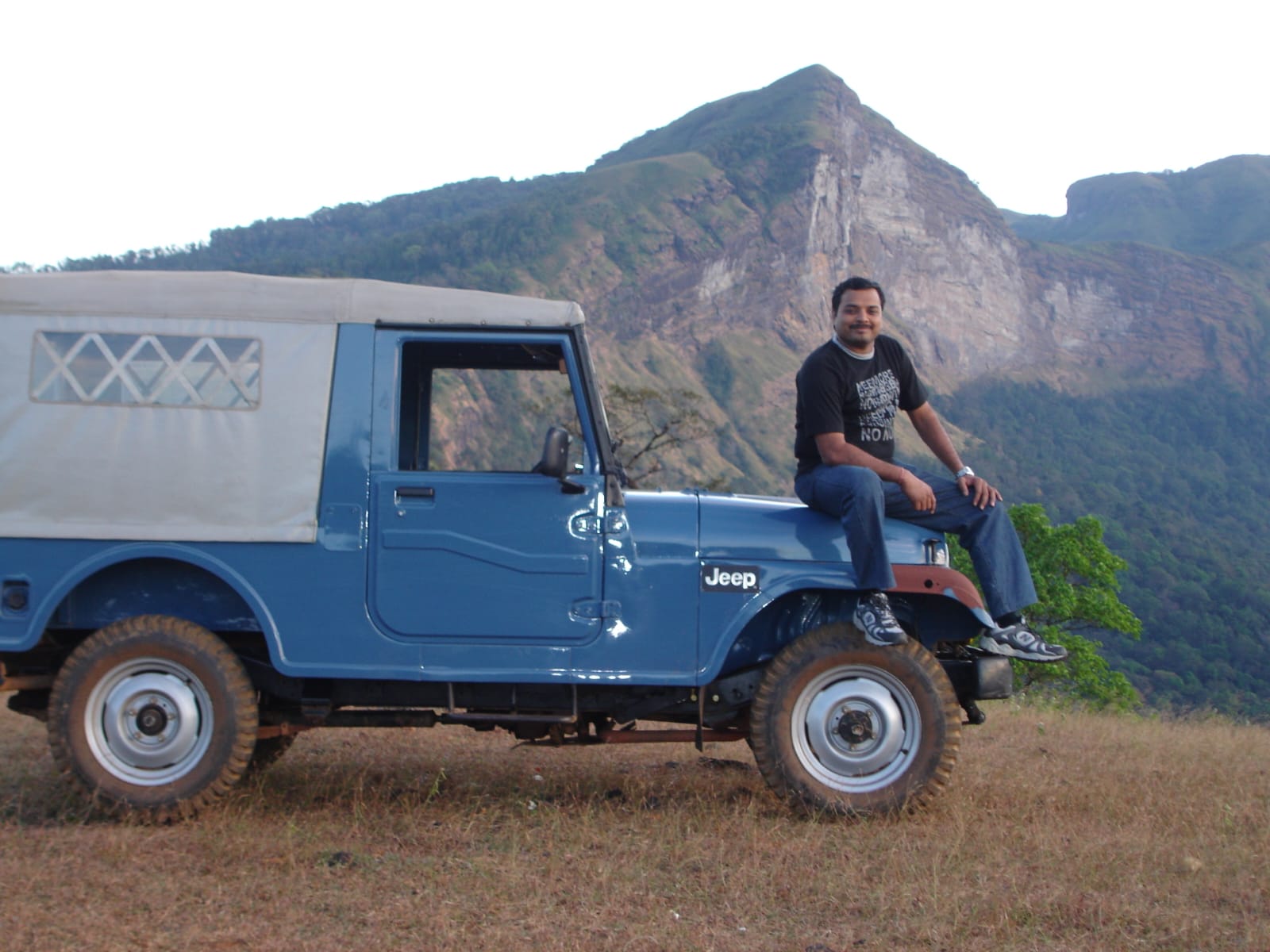KP sitting on a Jeep at a mountain viewpoint